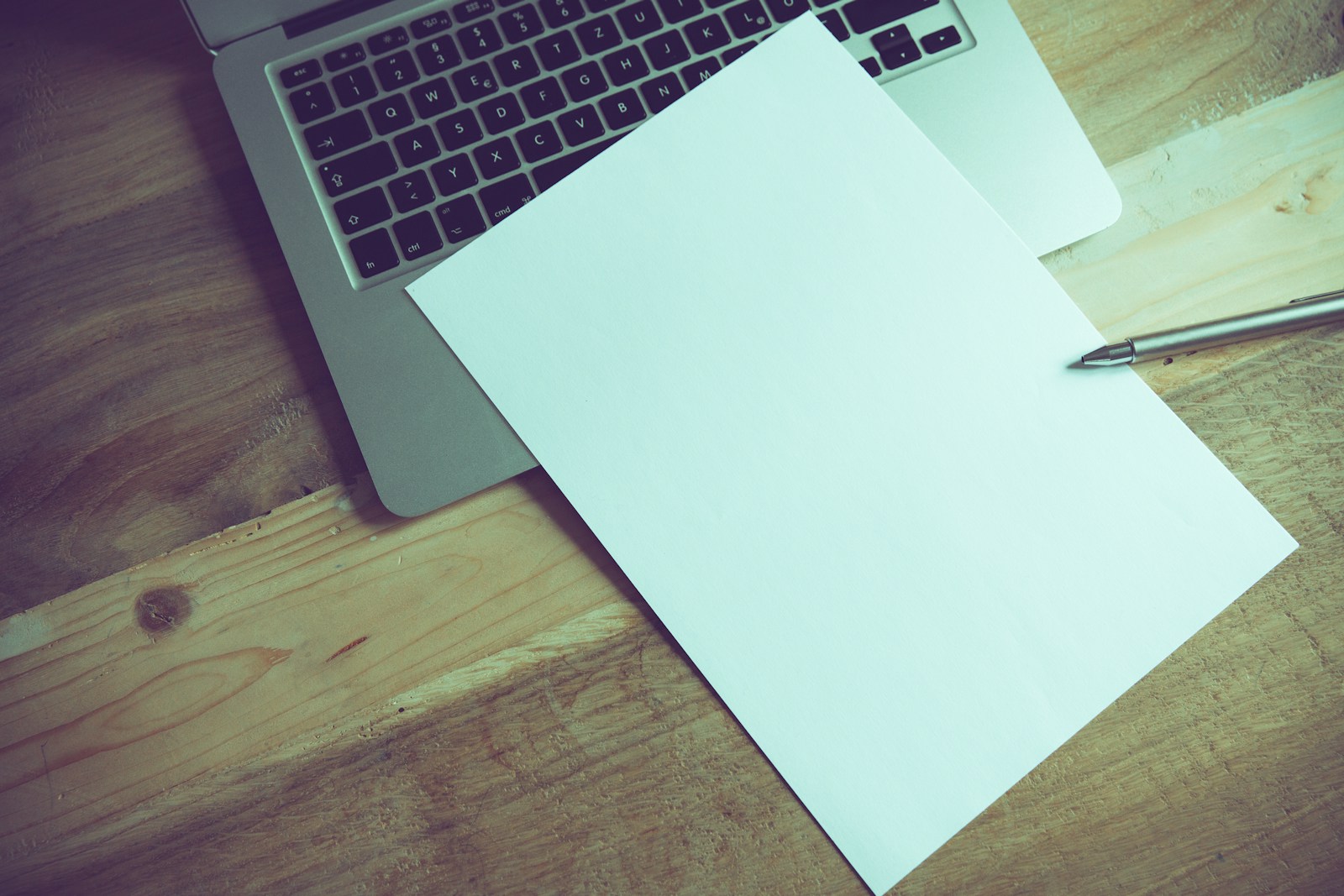 a laptop computer sitting on top of a wooden desk with a blank sheet of paper symbolizing a surety bond